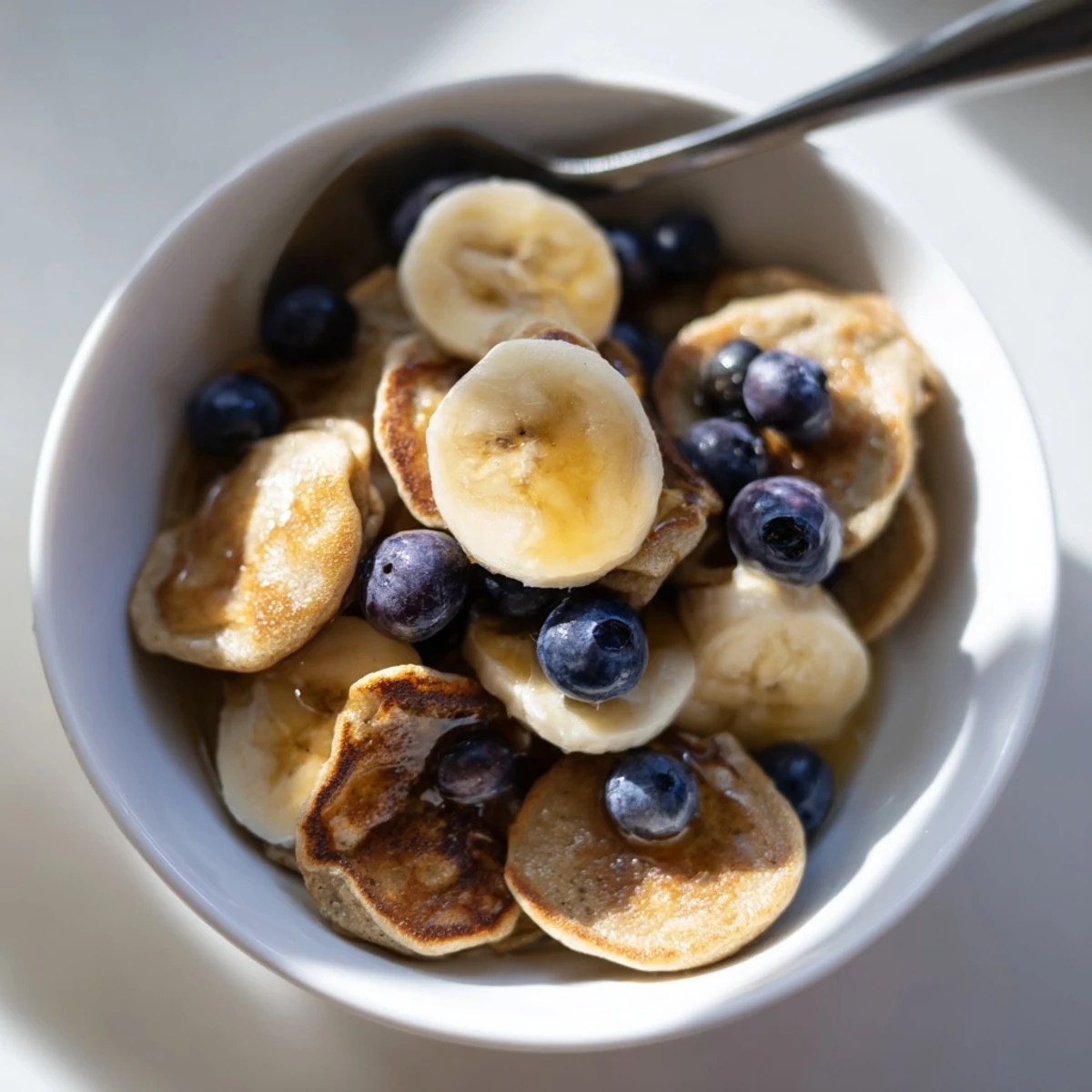 Adorable Mini Pancake Cereal served in a bowl with fresh berries and syrup.  