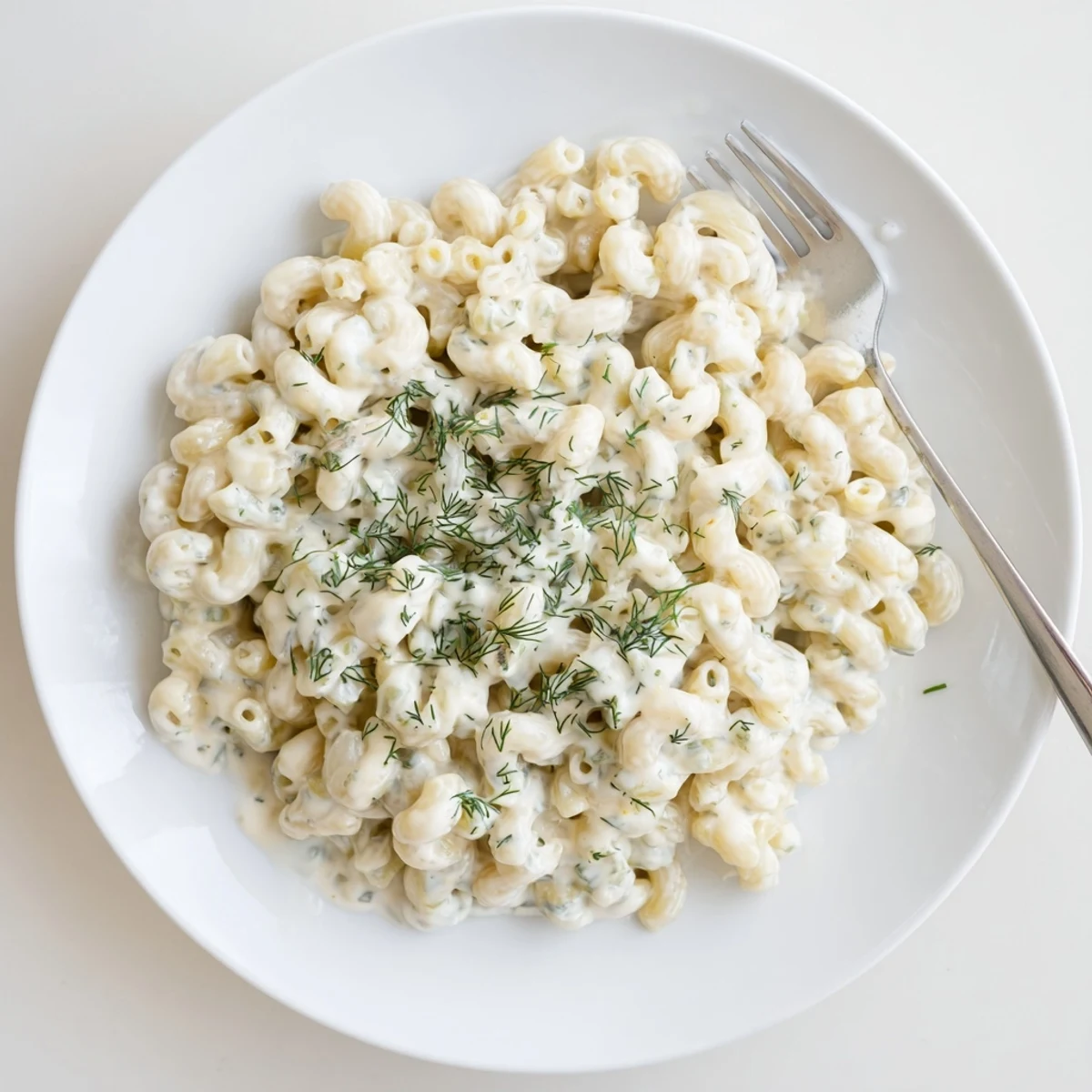 A steaming bowl of Pickle Mac and Cheese, its creamy sauce sprinkled with fresh dill.