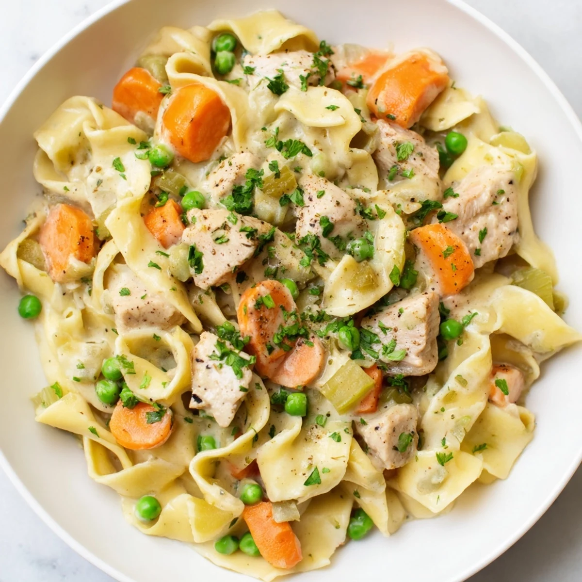 A close-up of creamy chicken and egg noodles, smelling of savory herbs and perfectly cooked.