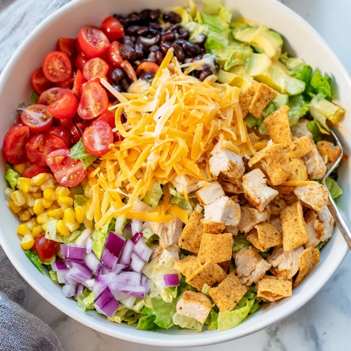Colorful chopped salad bowl with taco-seasoned chicken, black beans, corn, avocado, cheese, and crunchy tortilla chips, drizzled with creamy salsa ranch.  