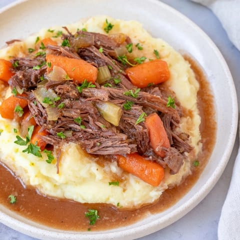 A close-up of a steaming bowl of slow cooker pot roast with creamy mashed potatoes.