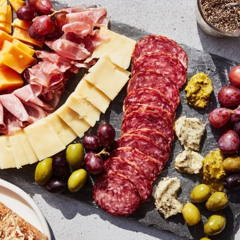 Straight lines of cold meats, sharp cheeses, and grapes comprise this Industrial Slate charcuterie board.