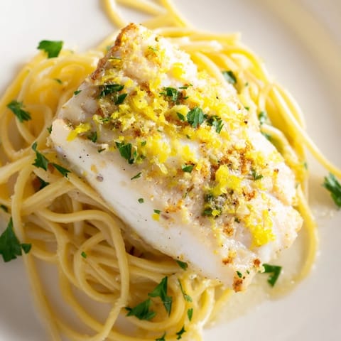 A close-up of zesty lemon bass pasta, featuring tender white fish and a vibrant, herb-flecked sauce.