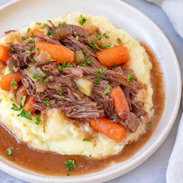 A close-up of a steaming bowl of slow cooker pot roast with creamy mashed potatoes.